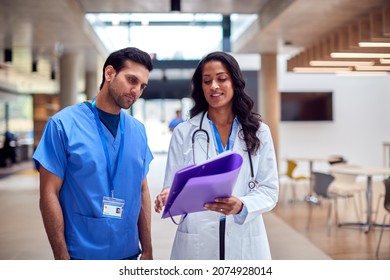 Medical Staff In White Coat And Scrubs Discussing Patient Notes Have Informal Meeting In Hospital - Powered by Shutterstock