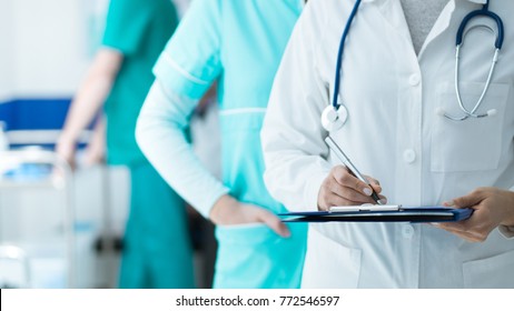 Medical Staff Working At The Hospital: Doctor And Nurse Checking A Patient's Medical Record On A Clipboard, Healthcare And Medical Exams Concept