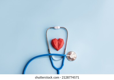 Medical stenoscope and red polygonal heart on a blue background. Minimal cardiology concept, copy space