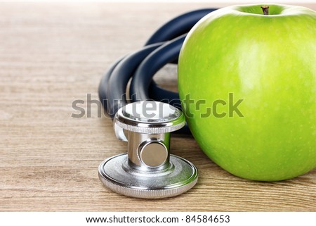 Medical stethoscope and apple on wooden background