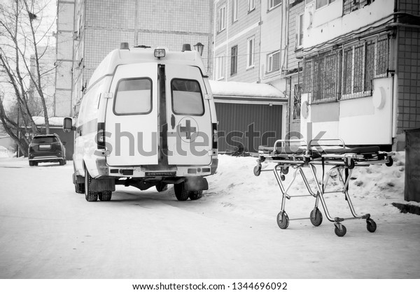 medical\
stretcher near to ambulance with open doors on the street near\
entrance of residential building -\
image.