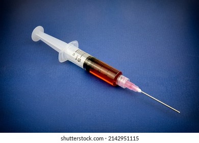 Medical syringe and needle on a tray with red liquid inside.