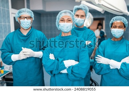 Medical team of confident successful surgeons in operating room standing with arms crossed and looking at camera as they pose together for a portrait, dressed professionally in operating gowns.