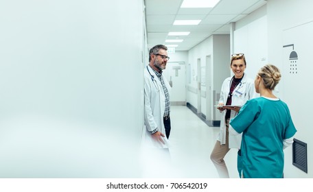 Medical team discussing in corridor at hospital. Mature doctor discussing with coworkers while standing in hospital hallway.