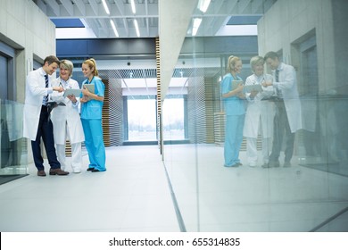 Medical Team Discussing Over Digital Tablet In Corridor At Hospital