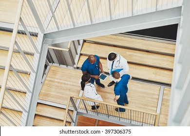 Medical Team Having An Emergency Discussion Standing Grouped In A Stairwell At The Hospital Looking Up Information On A Tablet,, View From Above Down The Stairwell