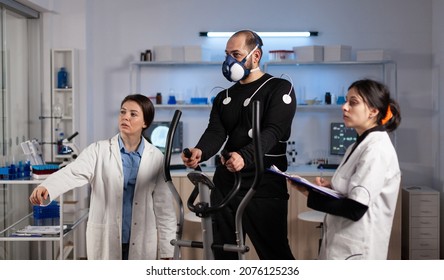 Medical team monitoring body endurance of sportman analyzing EKG data during medicine workout in modern laboratory. Athlete man with electrodes sensor on it running on fitness trainer - Powered by Shutterstock