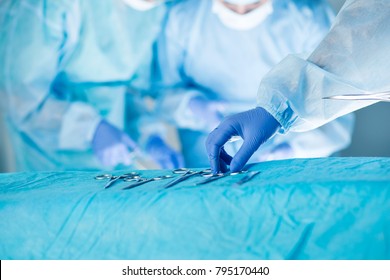 Medical team performing operation. Close up of scrub nurse taking medical instruments for operation with colleagues performing in background