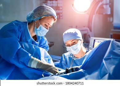 Medical Team Performing Surgical Operation In Bright Modern Surgery Room. Operating Theatre. Modern Equipment In Clinic. Emergency Room.