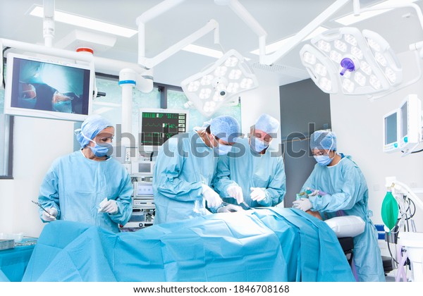 A medical team performing surgical operations while\
standing around some latest medical equipment and top end machinery\
in an operating suite