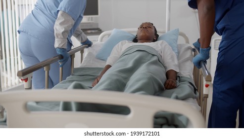 Medical team push emergency stretcher transporting afro woman patient in hospital. Sick unconscious female lying in hospital bed moved by doctors in hospital ward - Shutterstock ID 1939172101