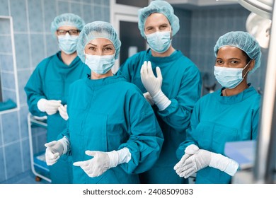 Medical team of surgeons ready for operation in operating room standing and looking at camera as they pose together for a portrait, dressed professionally in operating gowns. - Powered by Shutterstock