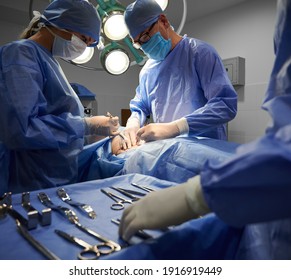 Medical team in surgical suits performing aesthetic surgery in operating room. Doctors doing cosmetic surgery while assistant standing by surgical table with medical tools. Concept of plastic surgery.