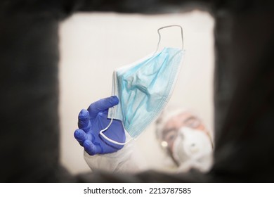 A Medical Technician Throws Away A Face Mask. Hand In Medical Gloves Throwing Out Discarded, Used Protective Masks In The Trash Bin After Quarantine