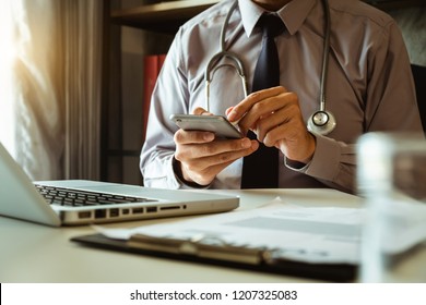 Konzept der Medizintechnik. Ärzte, die mit Mobiltelefon, Stethoskop und digitalem Tablet-Laptop arbeiten, im modernen Büro im Krankenhaus bei Morgenlicht
