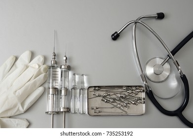 Medical Tools: Vintage Glass Syringes, Ampules, Needles In Box, Rubber Gloves And Stethoscope On Grey Background. Top View Point.