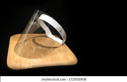 Medical visor lying on a wooden countertop on black background. Plastic full face cover visor. Protective shield mask used against diseases spread by droplet. 