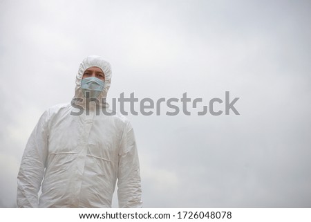 A medical worker, a doctor in a white protective suit and a blue face mask, wearing rubber latex gloves, stands on the street. Viral disease epidemic, coronavirus outbreak
