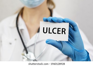 A medical worker in gloves holds a card with the words ULCER. Medical concept.