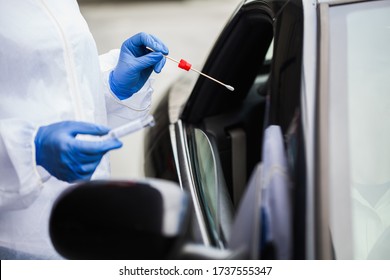 Medical worker in N95 PPE performing nasal throat swab on person in vehicle through car window,COVID-19 UK mobile testing centre drive thru facility,hands closeup in blue gloves holding test kit