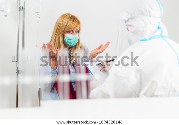 Medical worker in PPE in COVID-19 test hospital\
lab giving bad news to patient. Patient is upset, and doesn’t\
believe in the results.