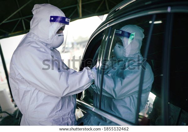 Medical worker in PPE performing\
nasal & throat swab on person in vehicle through car\
window,COVID-19 mobile testing centre. Turin, Italy - November\
2020