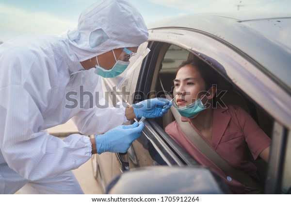 Medical\
worker in protective suit screening woman Driver to Sampling\
secretion to check for Covid-19. Drive thru test coronavirus fast\
track. Concept prevention coronavirus\
outbreak.