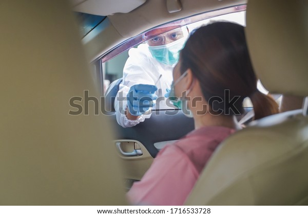 Medical\
worker in protective suit screening woman Driver to Sampling\
secretion to check for Covid-19. Drive thru test coronavirus fast\
track. Concept prevention coronavirus\
outbreak.