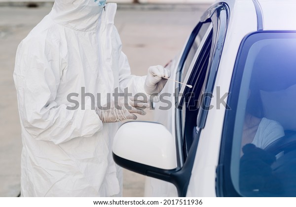 Medical worker in protective suit screening woman\
Driver to Sampling secretion to check for Covid-19. check,taking\
nasal swab specimen sample from male patient through car window,PCR\
diagnostic for Co
