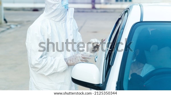 Medical worker in\
protective suit screening woman Driver to Sampling secretion to\
check for Covid-19. check,taking nasal swab specimen sample from\
patient through car 