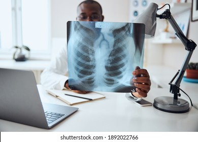 Medical Worker Stretching His Arm With A Chest Film And Carefully Examining It While Sitting At His Desk