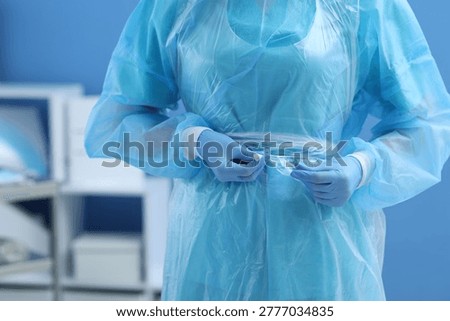 Medical worker tying disposable isolation gown indoors, closeup