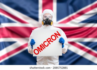 Medical worker wearing PPE protective white suit,face shield mask, holding text inscription omicron covid-19 SARS-CoV-2 Coronavirus B.1.1.529 new variant or strain behind blur uk united kingdom flag