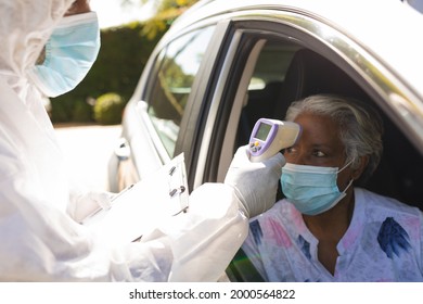 Medical Worker Wearing Ppe Suit Taking Temperature Of Senior African American Woman Sitting In Car. Retirement And Senior Lifestyle During Covid 19 Concept.