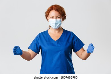 Medical Workers, Covid-19 Pandemic, Coronavirus Concept. Happy Smiling And Amazed Female Doctor, Nurse In Scrubs And Face Mask, Spread Hands As If Holding Something Big, Show Large Size