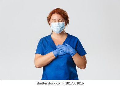 Medical Workers, Covid-19 Pandemic, Coronavirus Concept. Happy And Dreamy Redhead Female Nurse, Middle-aged Doctor In Face Mask And Gloves Close Eyes, Press Hands To Heart, Daydreaming, Keep In Mind