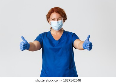 Medical Workers, Covid-19 Pandemic, Coronavirus Concept. Happy Smiling Female Doctor, Middle-aged Nurse In Medical Mask And Gloves Showing Thumbs-up, Gurantee Quality Service At Clinic