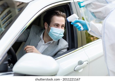 Medical workers measuring temperature with thermometer outdoors. Pandemics and epidemics prevention. Paramedic in hazmat suit checks of young man driver in protective mask through open window - Powered by Shutterstock