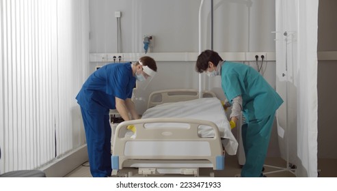 Medical workers in safety mask and gloves changing bed sheets in hospital room. Nurse team in protective uniform cleaning hospital ward after covid-19 patient recovery - Powered by Shutterstock