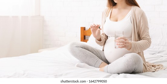 Medicaments during pregnancy. Pregnant woman taking vitamin pill, panorama, free space