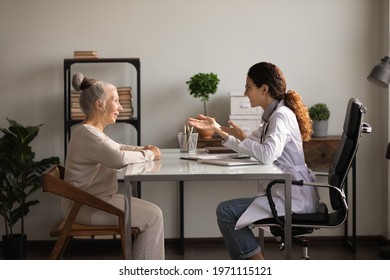 Medicare for older people. Friendly hispanic woman gp family therapist consult elderly female patient at meeting at hospital cabinet. Old lady retiree visit doc listen to recommendation for treatment - Shutterstock ID 1971115121