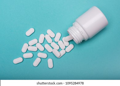 Medication bottle and white pills spilled on blue pastel coloured background. Medication and prescription pills flat lay background. Opioid epidemic.