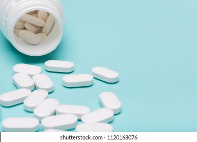 Medication bottle and white pills spilled over blue pastel colored background. Medication and prescription pills background. Pharmaceutical drugs.