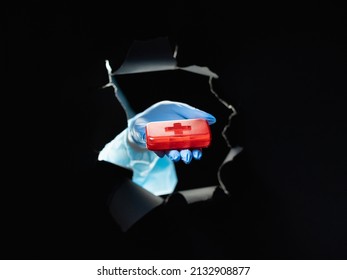 Medication Dosage. Prescription Drug. Pharmaceutical Meds. Doctor Hand In Blue Glove Holding Red Cross Pill Box Organizer Inside Black Breakthrough Hole Torn Wall Isolated On Dark.