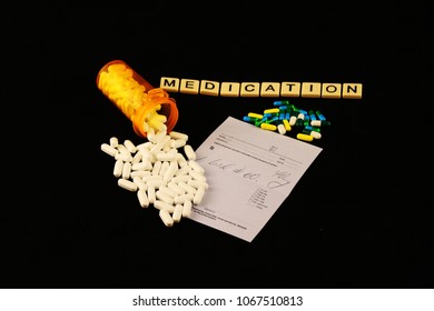 Medication Is Spelled Out With Tiles Over A Spilled Prescription Bottle Of White Pills And Some Colored Pills Over A Prescription Pad On A Black Background