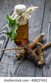 Medicinal plant - a burdock. The roots and leaves of burdock, burdock oil in bottle on a wooden background. It is used for the treatment and care of hair