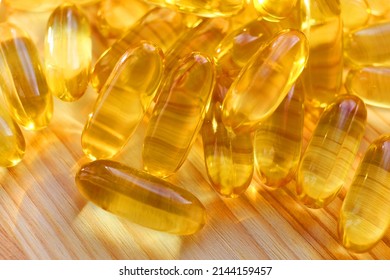 Medicinal Product Of Animal Origin Natural Purified Fish Oil In Large Yellow Transparent Capsules On Light Brown Wooden Surface Close-up. Fat Soluble Vitamin