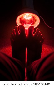 medicinal red-light-lamp radiating at a womans feet, dark colours