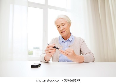 Medicine, Age, Diabetes, Health Care And People Concept - Happy Senior Woman With Glucometer Checking Blood Sugar Level At Home