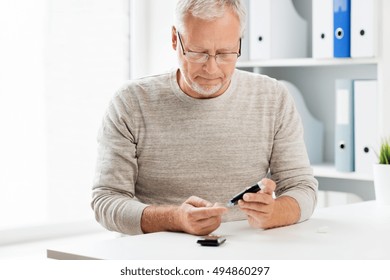 Medicine, Age, Diabetes, Health Care And Old People Concept - Senior Man With Glucometer Checking Blood Sugar Level At Home